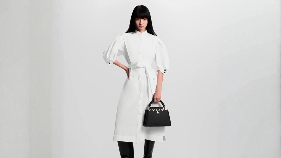 Woman in a white dress holding a black Louis Vuitton Capucines bag.