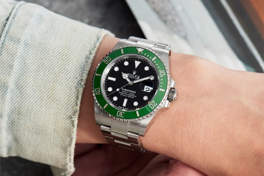 Rolex Submariner with green bezel worn on the wrist, featuring stainless steel bracelet and black dial.