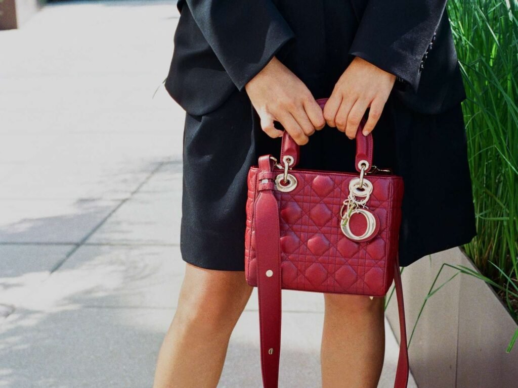 Woman holding a red Lady Dior handbag with quilted leather and charm details.