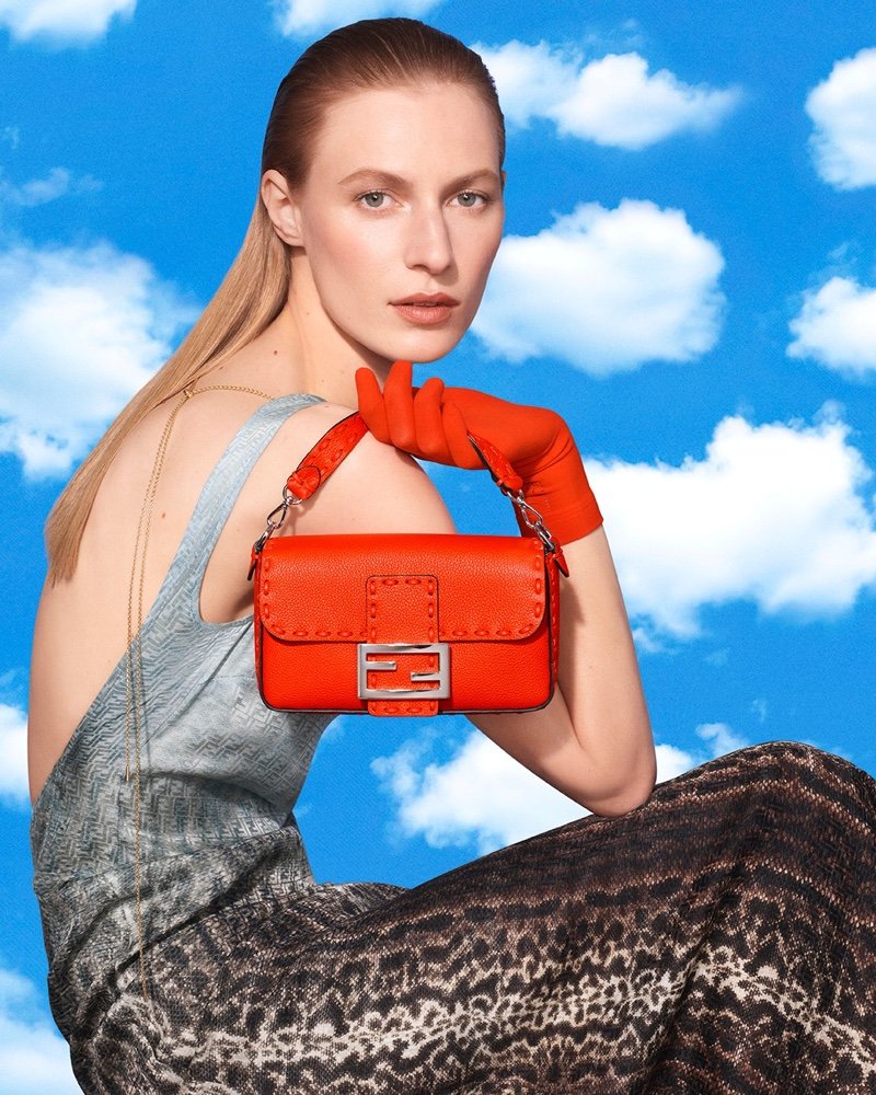 Model holding a red Fendi Baguette bag against a blue-sky backdrop.