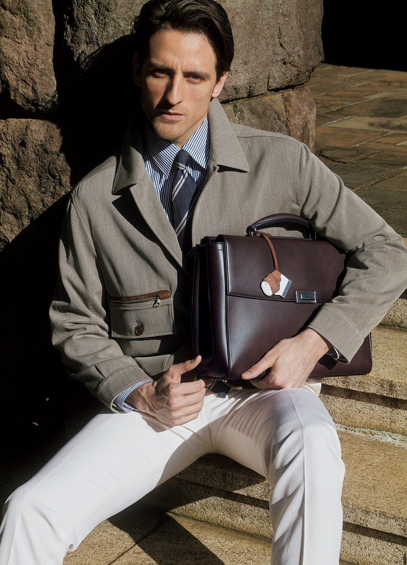 Model in tailored clothing holding a dark brown Dunhill leather briefcase.