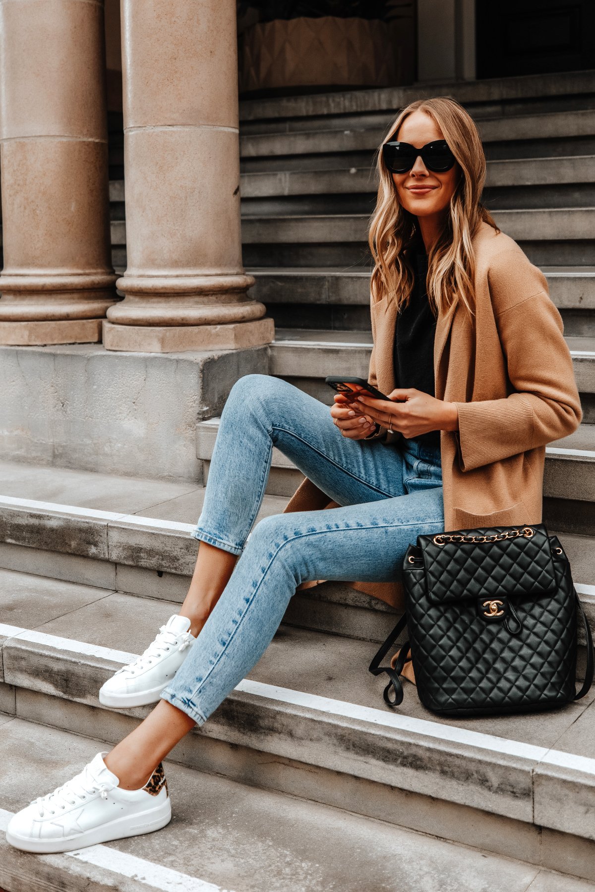 Model styling white Golden Goose sneakers with denim and a camel coat