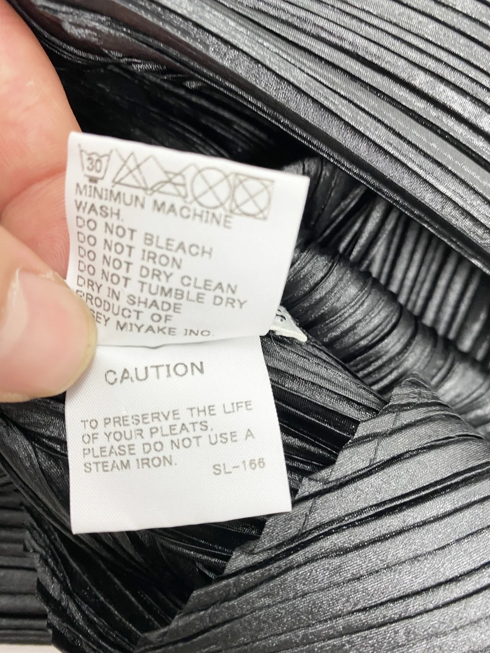 Pleats Please garment care label showing washing and heat instructions