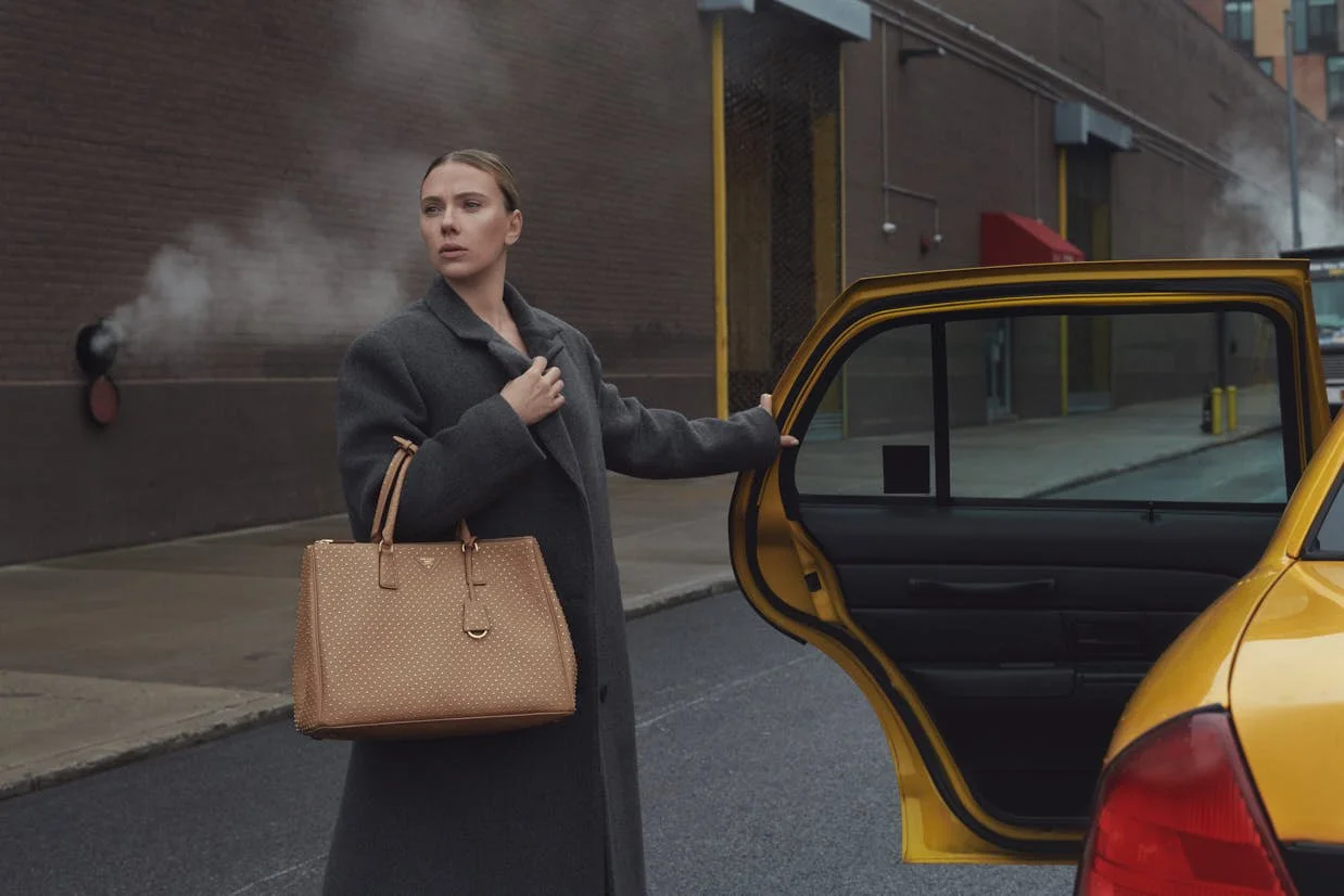 Woman stepping from a taxi while carrying a tan Prada Galleria handbag.