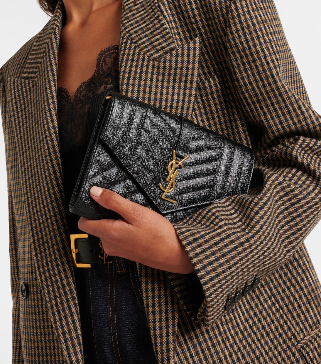 Model holding a black Saint Laurent Cassandre envelope clutch with a tailored checked blazer.