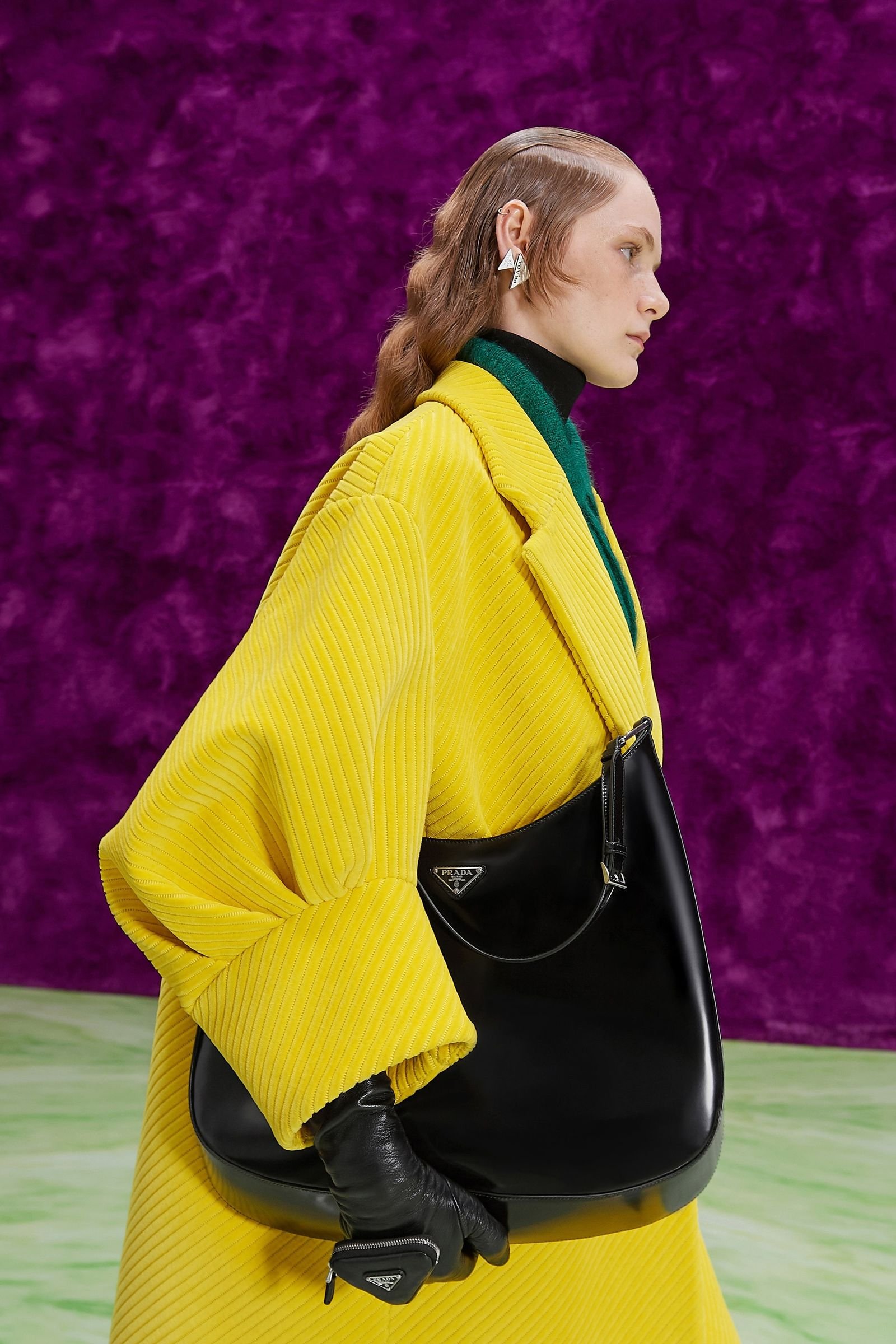 Model in a yellow coat carrying a black Prada Cleo shoulder bag.