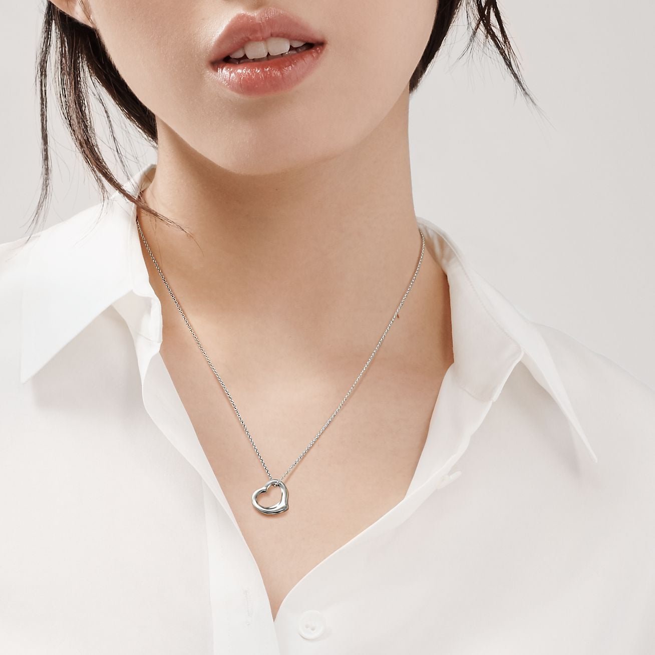 Model wearing a sterling-silver Elsa Peretti Open Heart necklace with a white shirt.