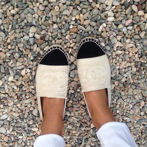 Chanel espadrilles worn with white trousers on a pebbled surface.