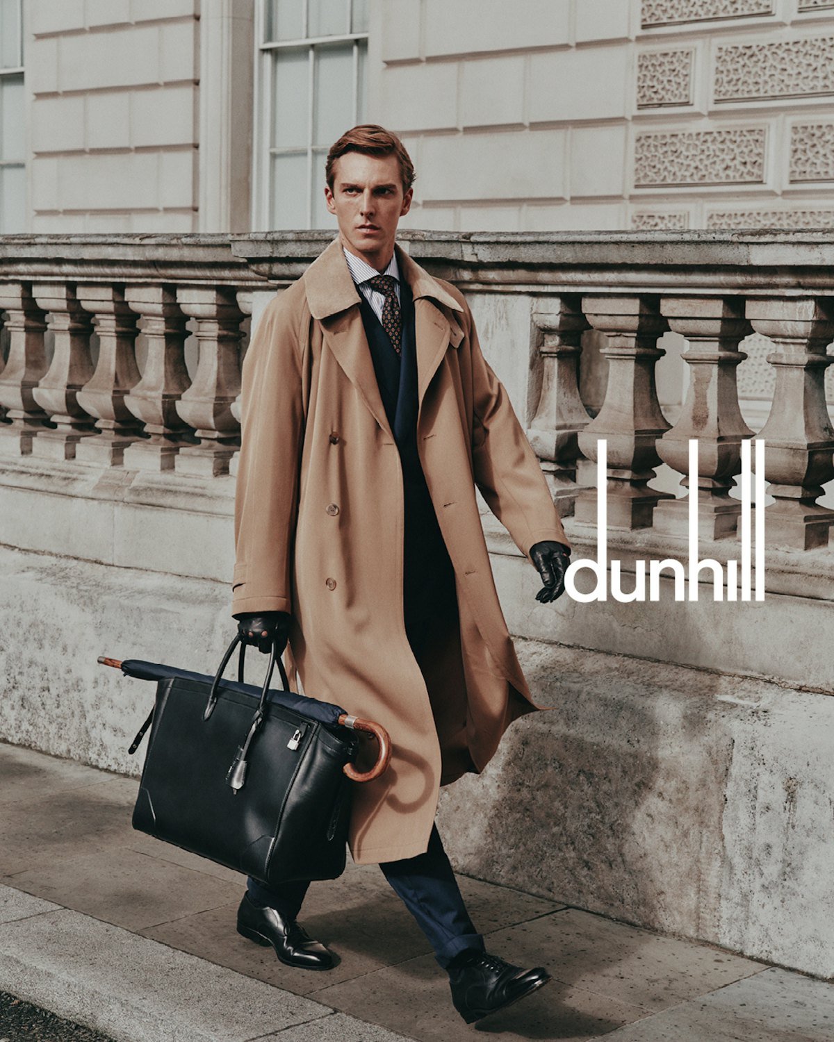 Model carrying a structured black Dunhill leather briefcase in a city setting.
