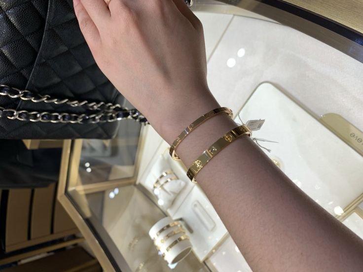 Small and classic yellow-gold Cartier Love Bracelets compared on the wrist.