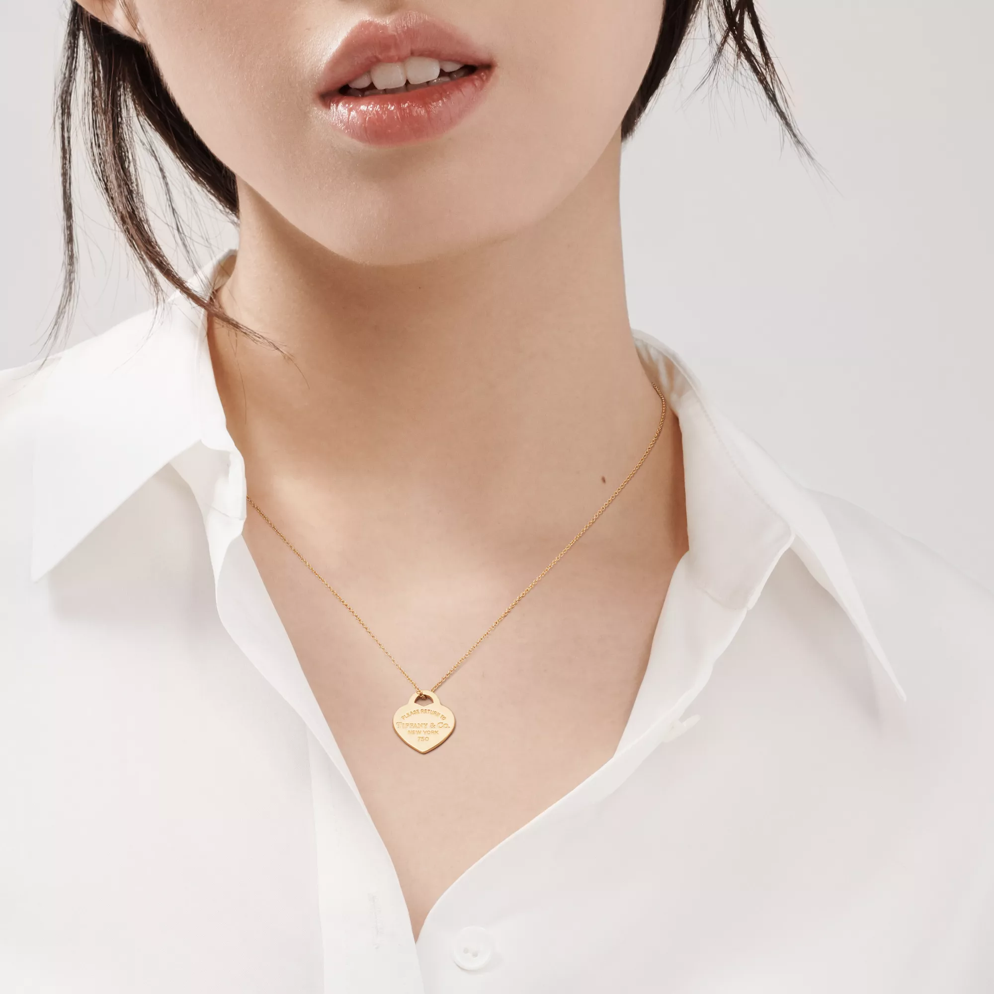 Model wearing a yellow-gold Return to Tiffany heart pendant over a white shirt.