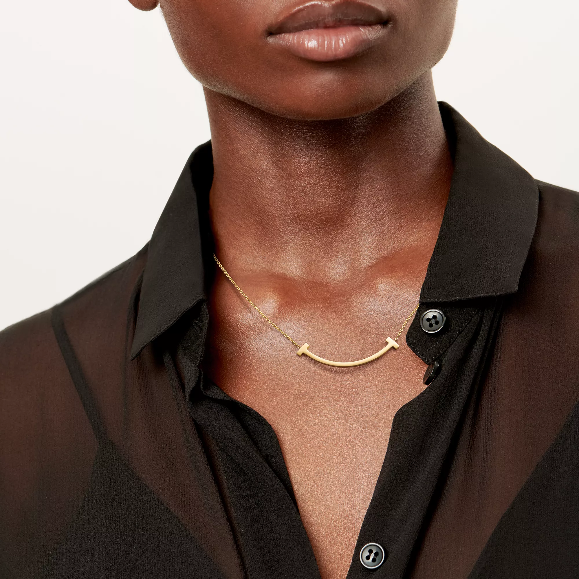 Model wearing a medium yellow-gold Tiffany T Smile pendant with a black blouse.