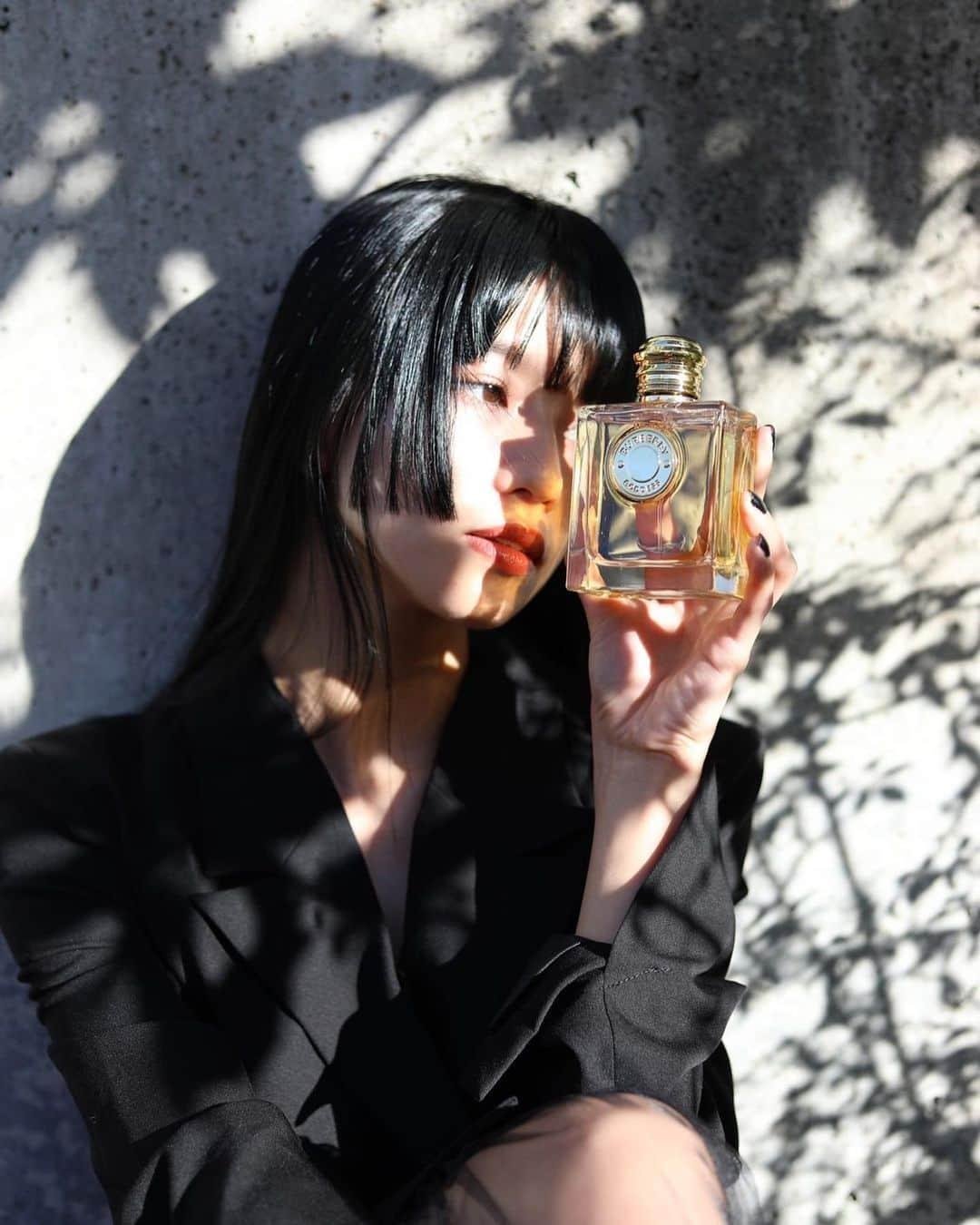 Model holding a Burberry Goddess fragrance bottle in warm natural light.