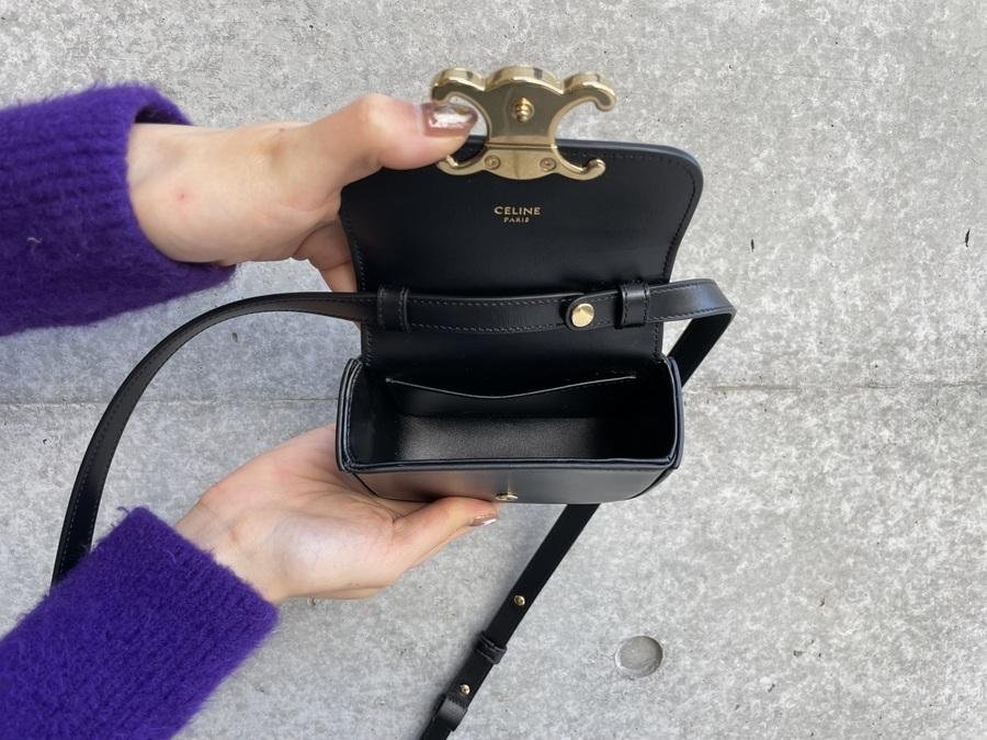 Hands opening the structured flap and Triomphe clasp of a black Celine bag.