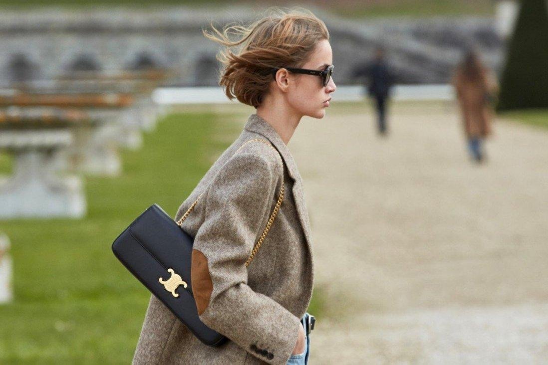 Model carrying a Celine Triomphe bag high on the shoulder outdoors.