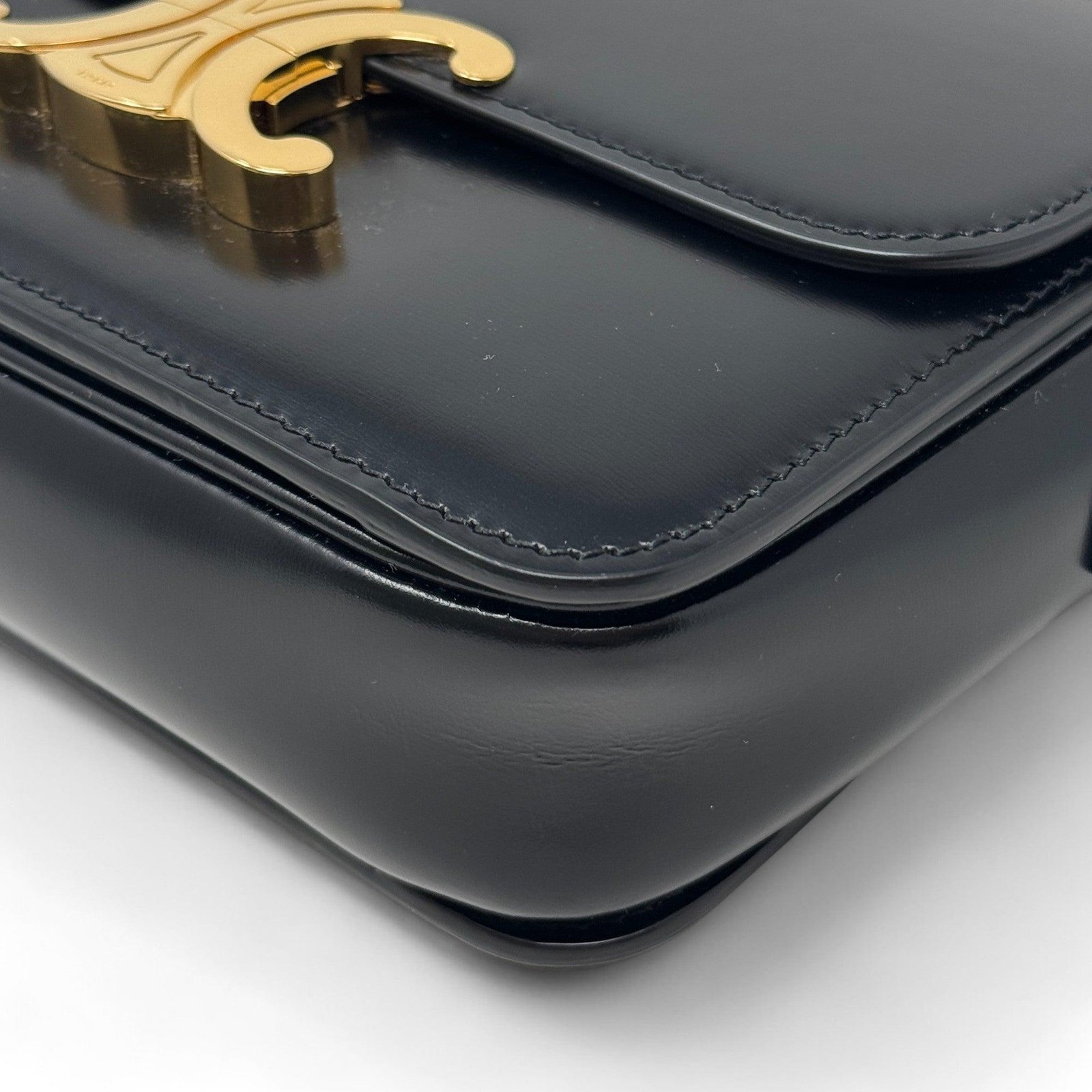 Close view of the curved corner and polished leather surface of a Celine Triomphe bag.