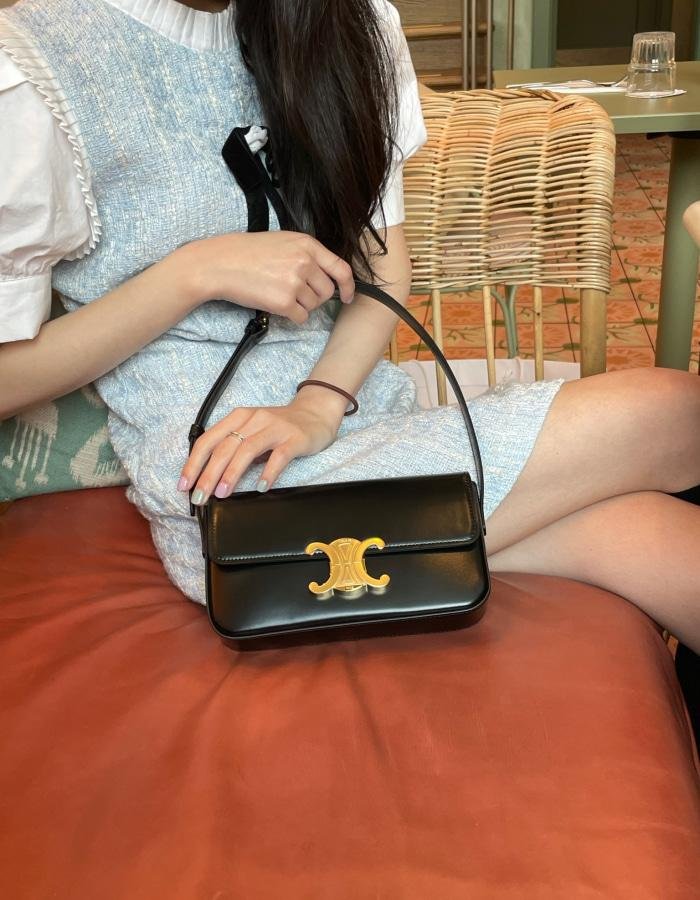 Model carrying a black Celine Triomphe bag with a relaxed daytime outfit.