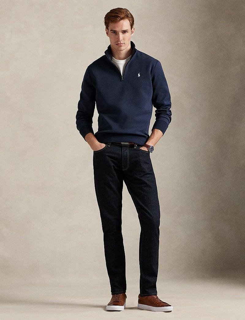 Model styling a navy Ralph Lauren quarter-zip with dark trousers.