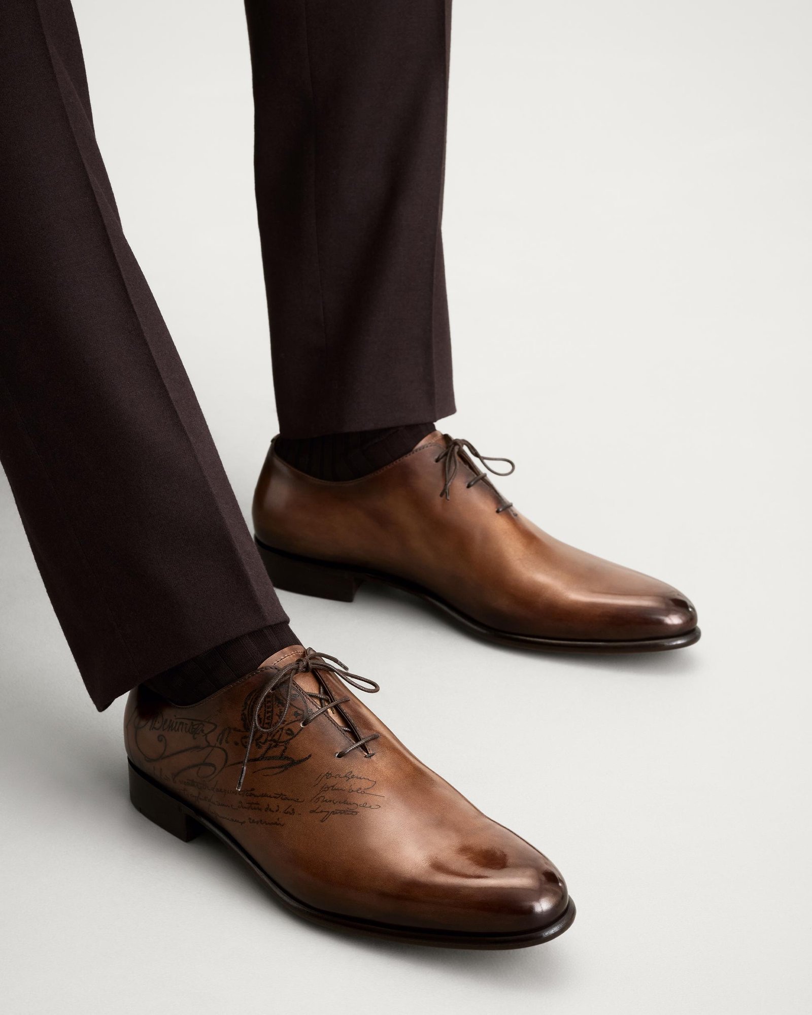 Brown Berluti Alessandro Oxford shoes displayed with leather-care accessories.