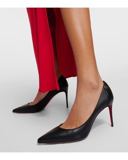 Black Christian Louboutin lower-heel pumps worn with red trousers.
