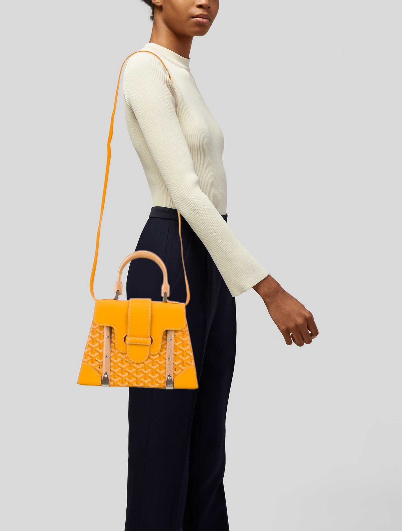 Woman carrying a bright Goyard Saïgon Mini bag by its wooden top handle.