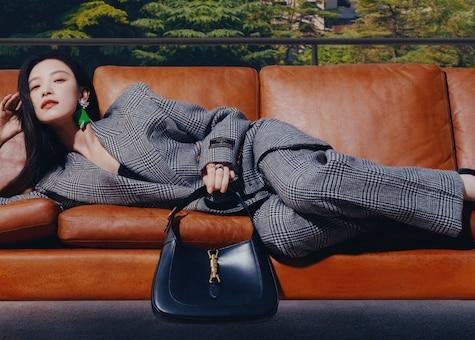 Model reclining beside a black Gucci Jackie 1961 bag in a campaign setting.