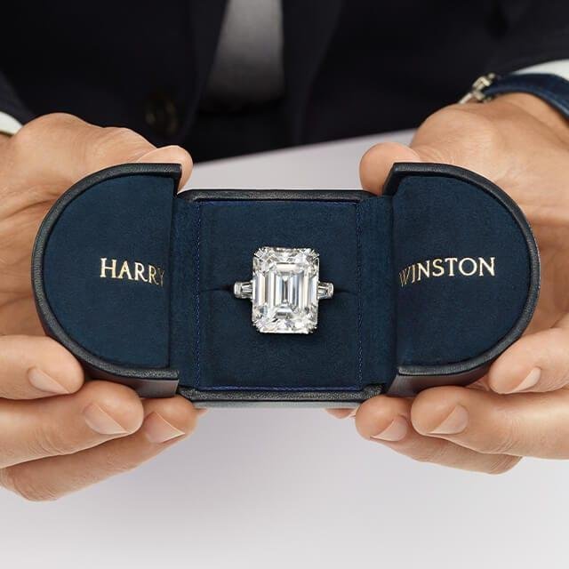 Harry Winston emerald-cut diamond engagement ring presented in a navy-blue box.