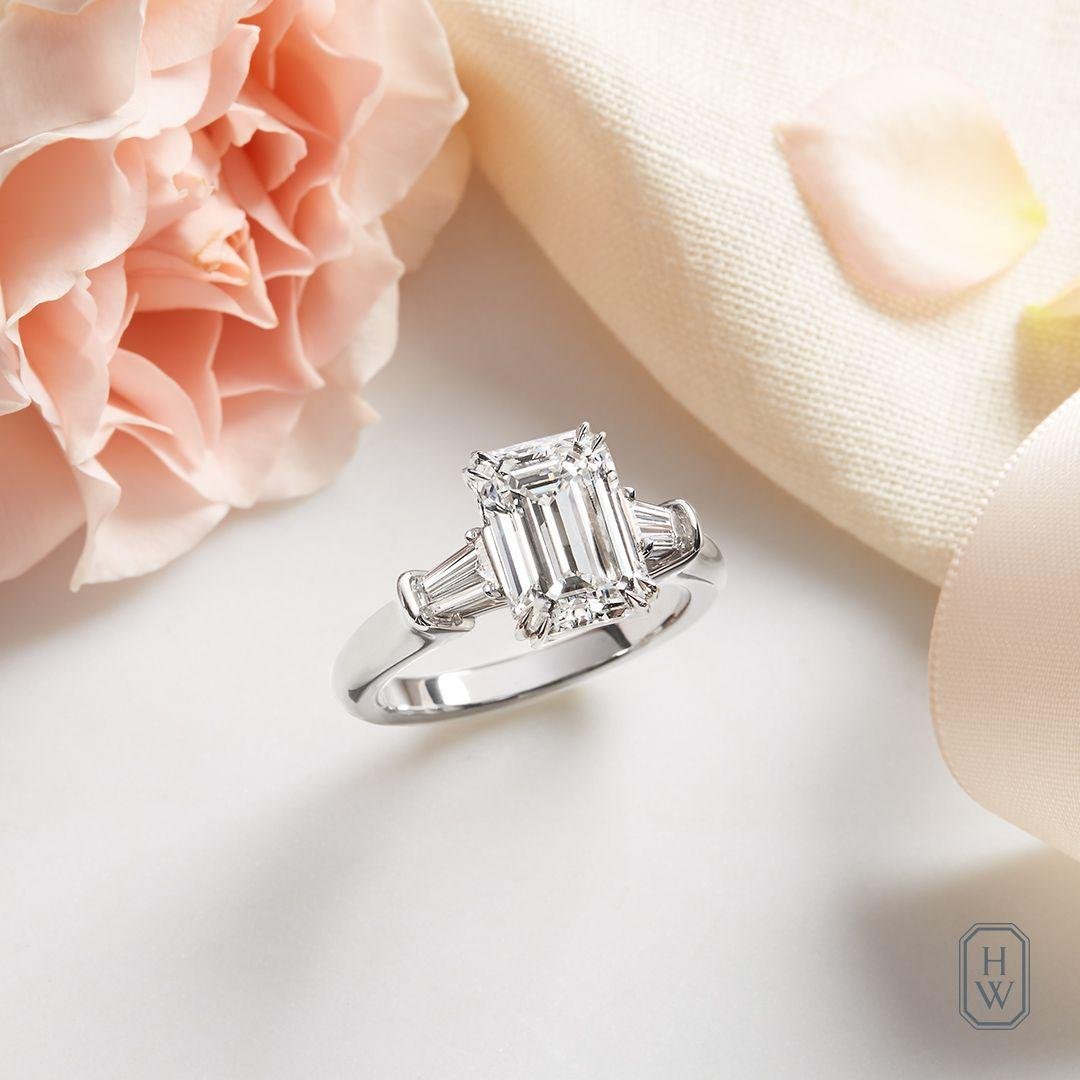 Harry Winston emerald-cut diamond engagement ring styled with pale flowers.