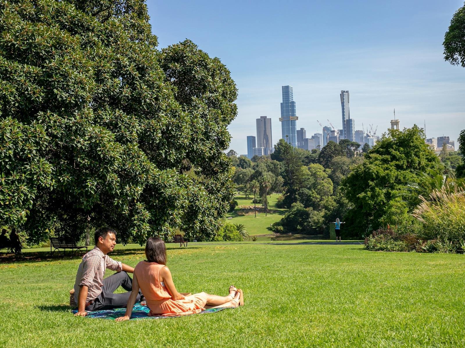 Visitors relaxing on a broad lawn with Melbourne’s skyline beyond.