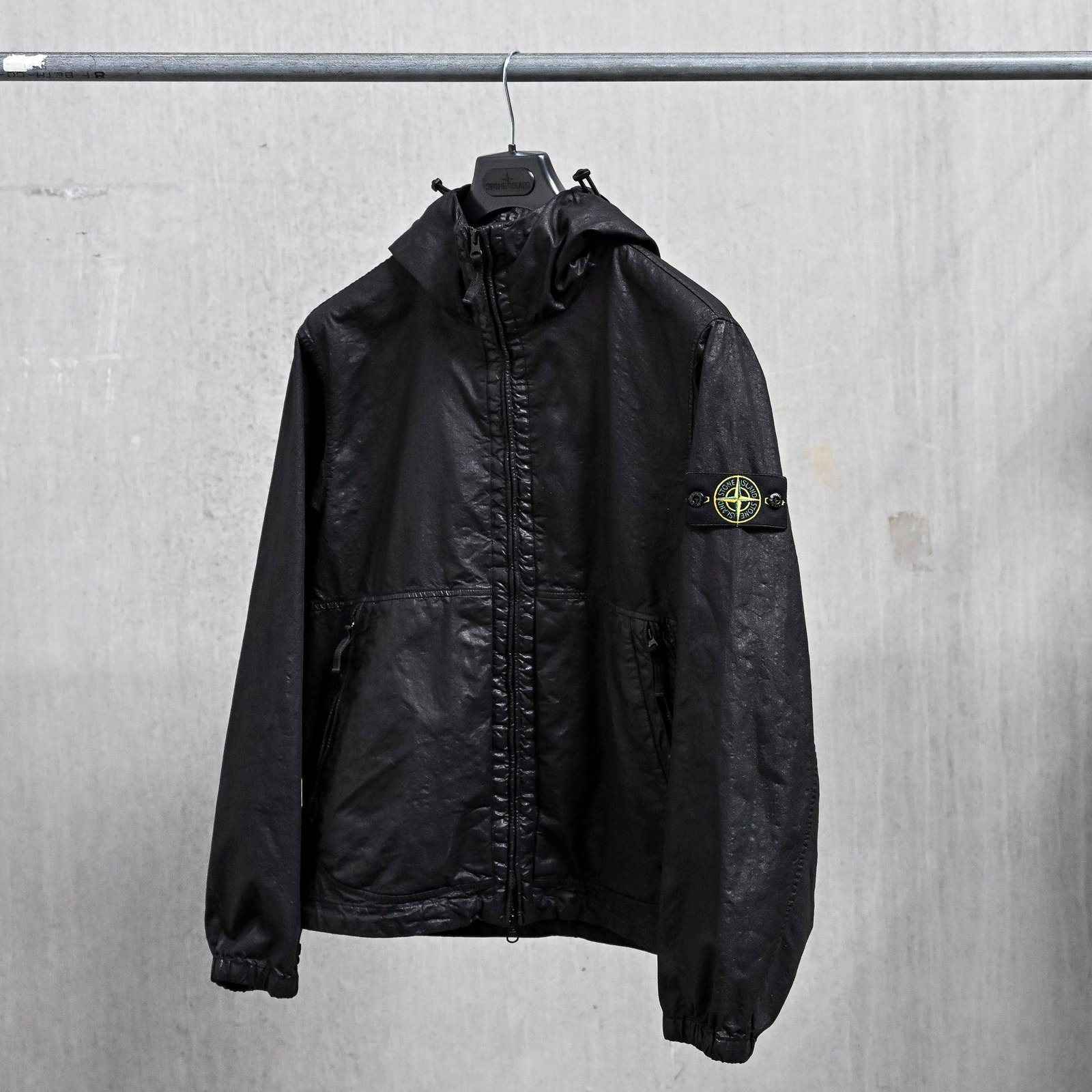Olive Stone Island technical jacket photographed against an industrial background.