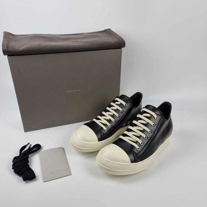 Black-and-milk Rick Owens sneakers in a dark editorial setting.