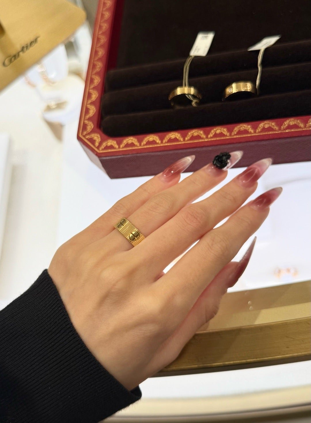 Hand trying on Cartier LOVE rings beside a red jewellery box.