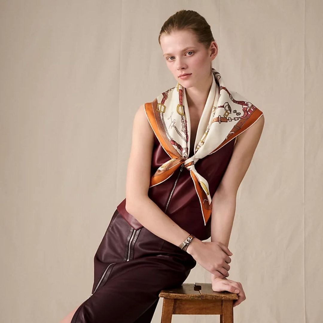 Model wearing a cream and orange Hermès Carré 90 scarf with a burgundy dress.