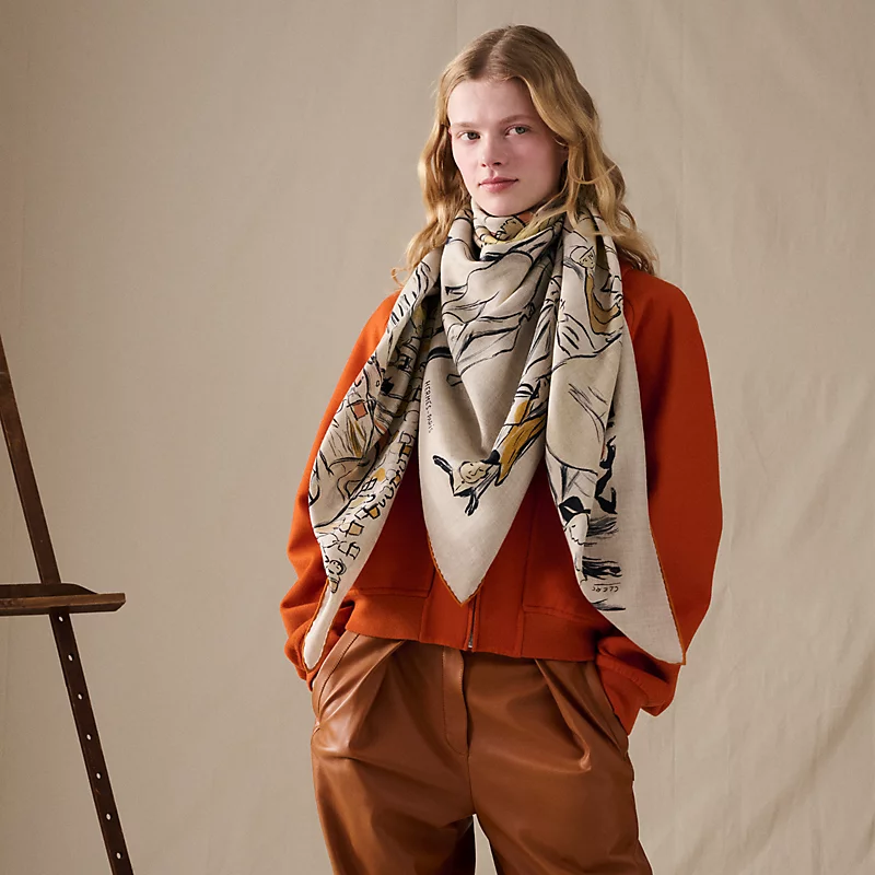 Model wearing a beige Hermès cashmere and silk shawl over brown clothing.