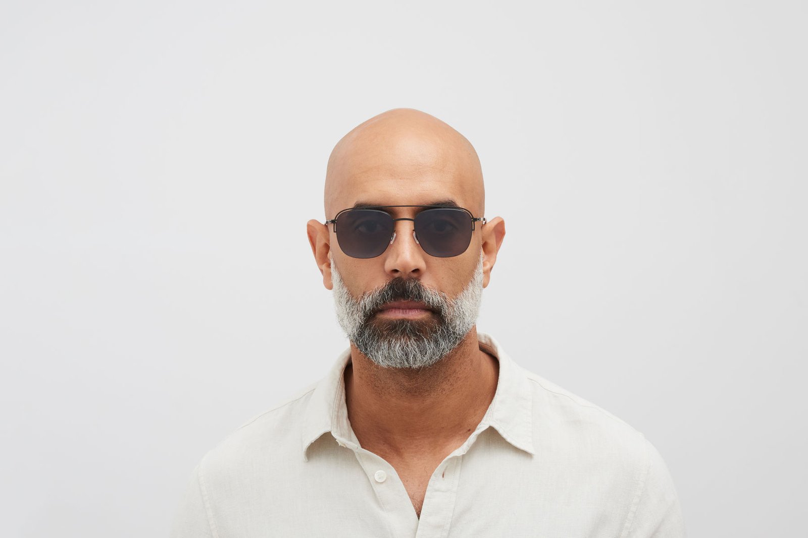 Model styling MYKITA NOR sunglasses with a pale open-collar shirt.
