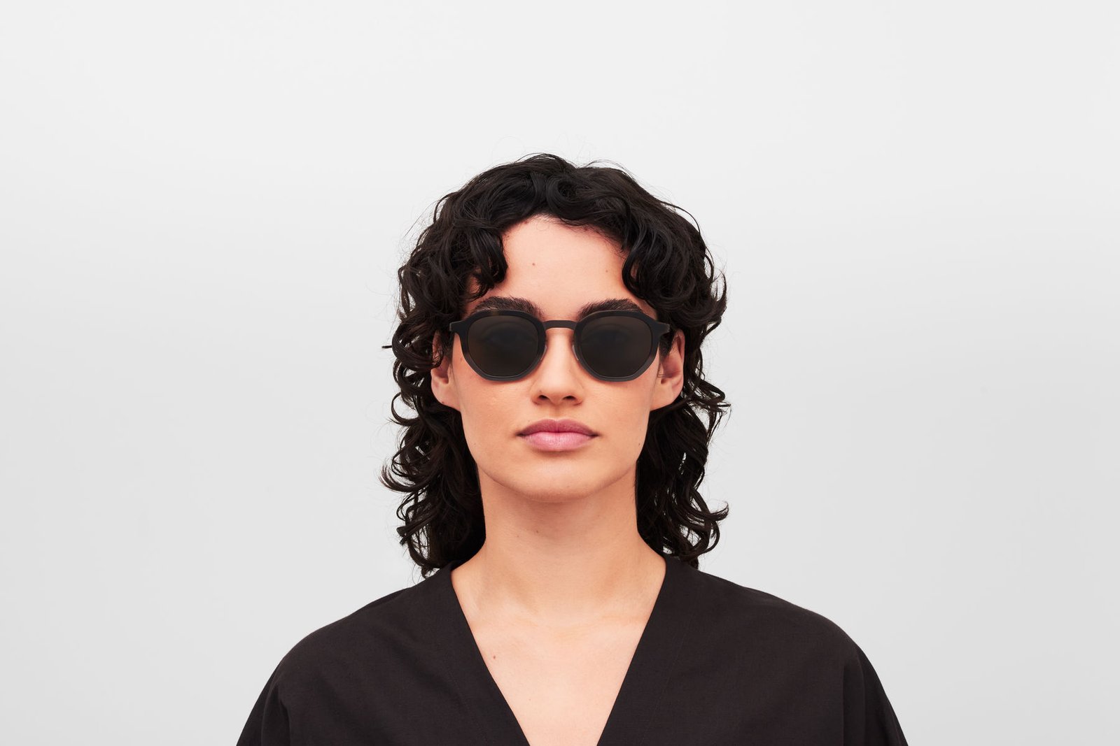 Model wearing MYKITA SAWYER sunglasses with a black open-neck top.