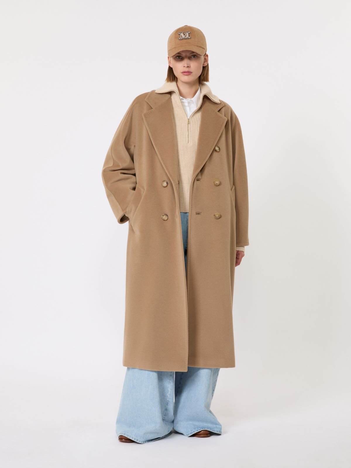 Model wearing a camel wool coat over a shirt with pale blue jeans.