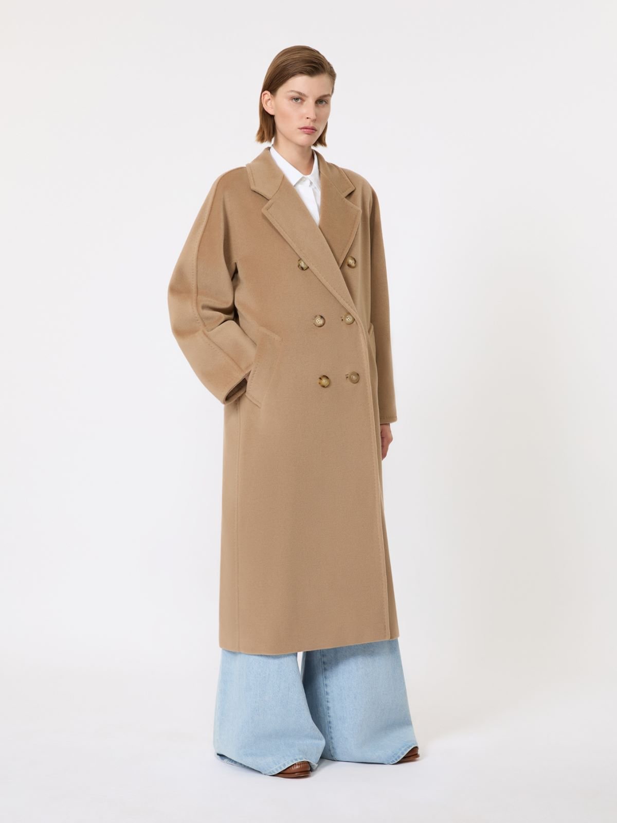 Model pairing a camel overcoat with a white shirt and relaxed jeans.