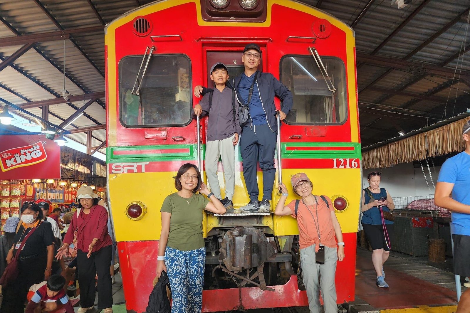 Visitors beside a red train at Maeklong Railway Market.