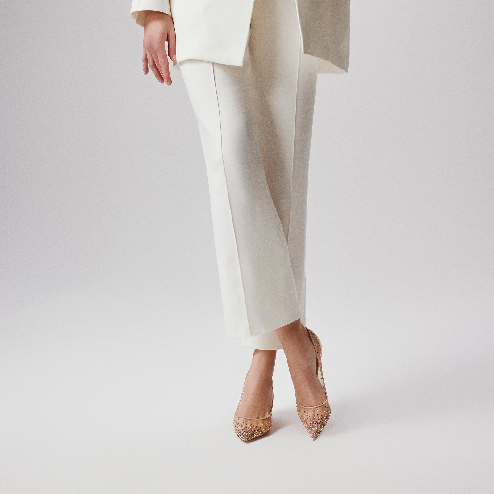 Model wearing crystal mesh pumps with cream tailored trousers