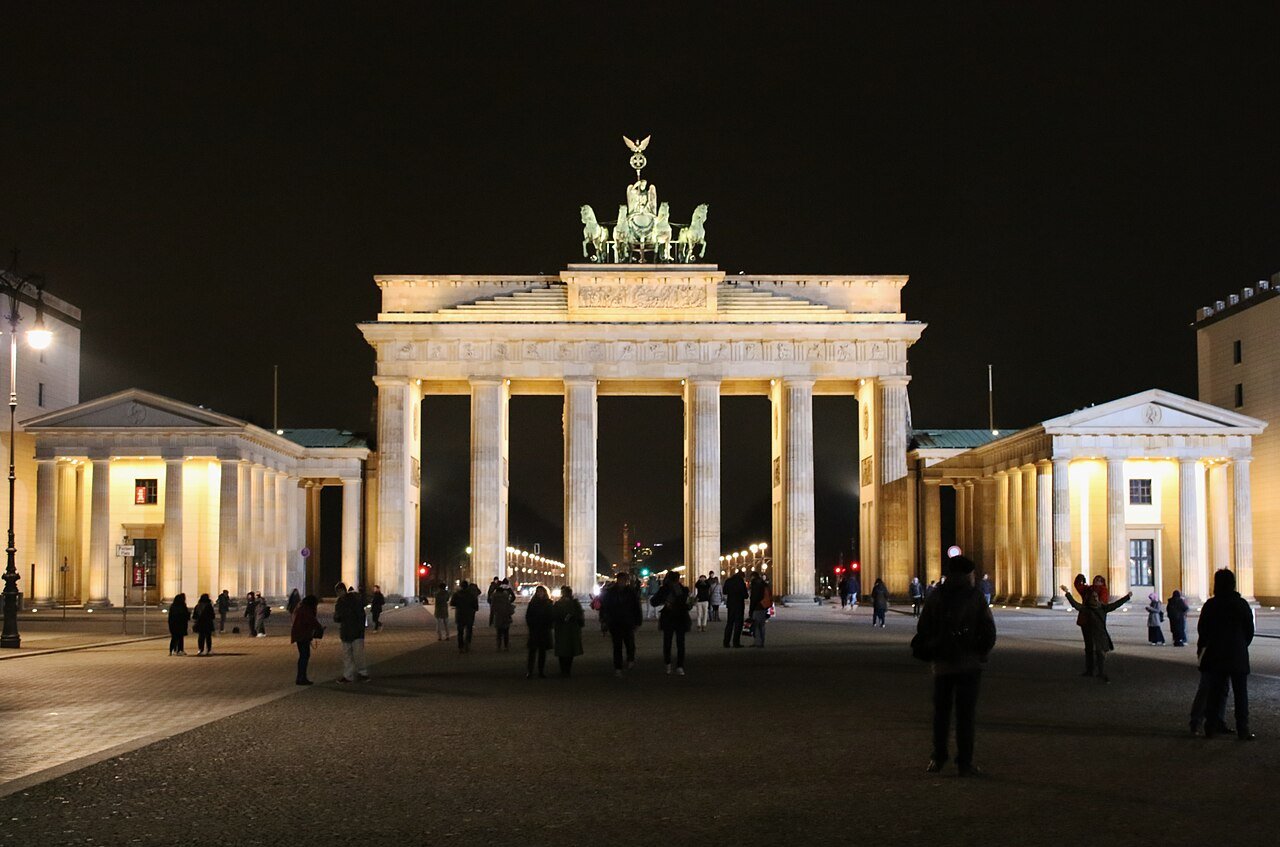 Pedestrians in the open space before Brandenburg Gate at night.