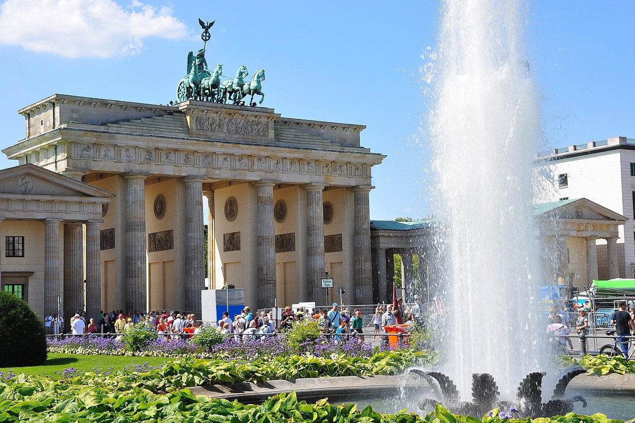 Brandenburg Gate in daylight with flowers and a fountain in the foreground.