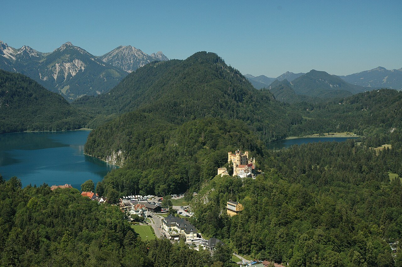 Hohenschwangau village and castle between Alpine lakes and wooded mountains.