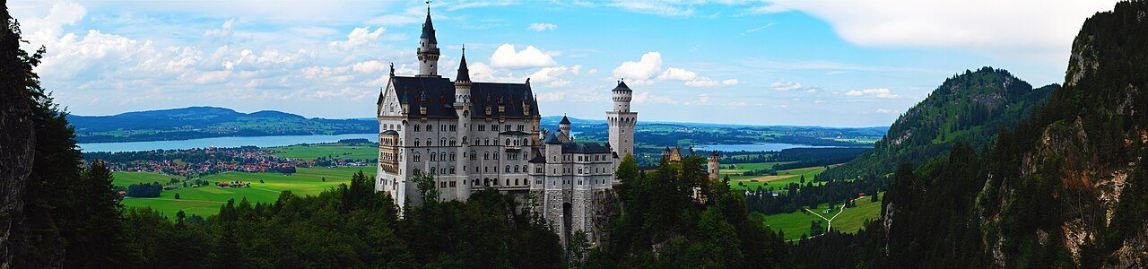 Panoramic view of Neuschwanstein Castle against the surrounding mountains and countryside.