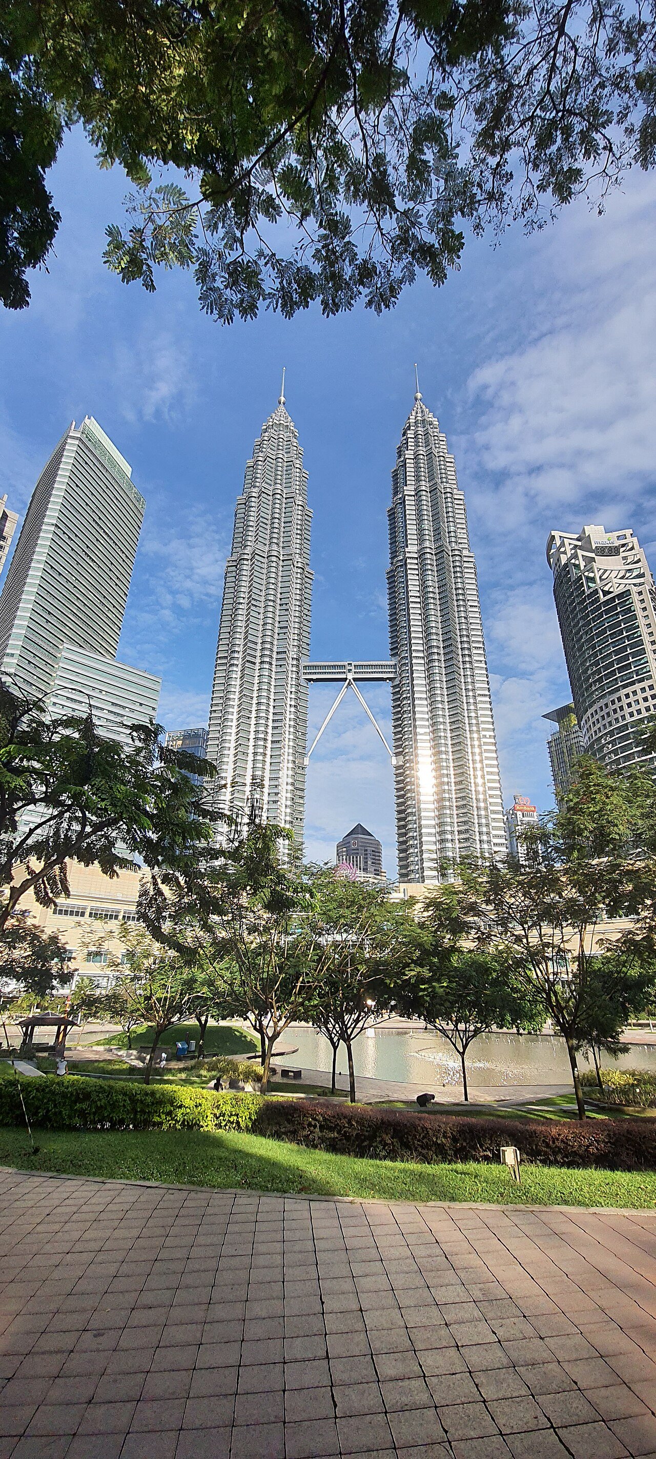 Petronas Twin Towers framed by trees and a pedestrian path in KLCC Park.