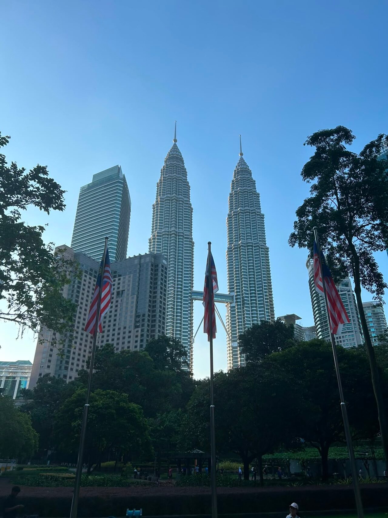 Petronas Twin Towers rising above trees near the Kuala Lumpur Convention Centre.