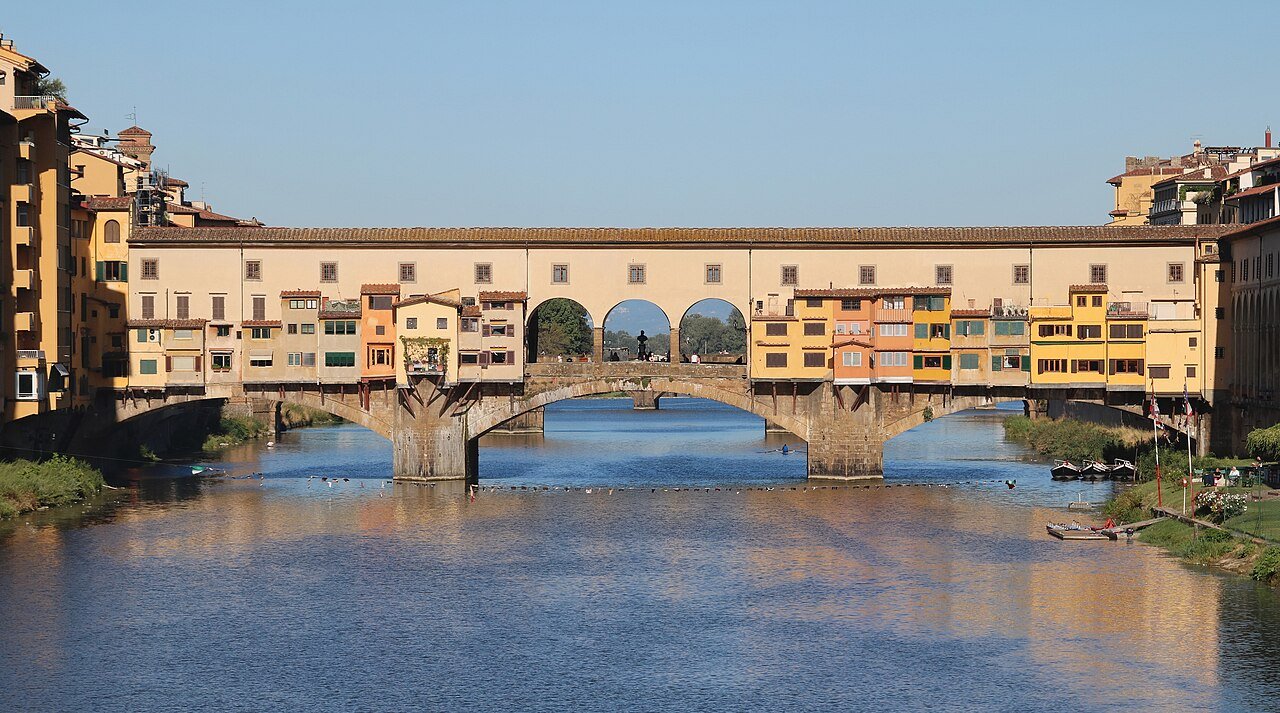 Ponte Vecchio’s jewellery shops and stone arches reflected in the Arno River in Florence.