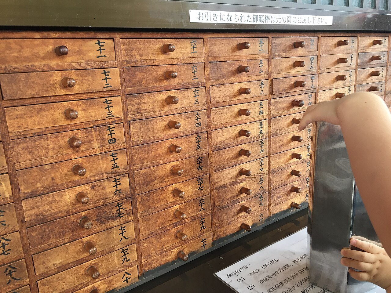 A visitor drawing a fortune stick beside Senso-ji’s omikuji drawers.