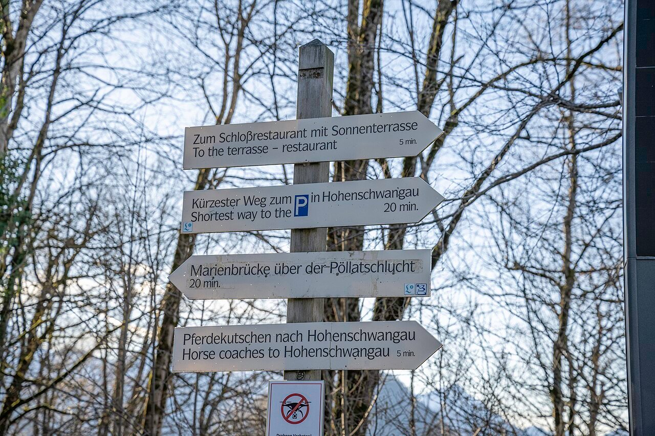 Visitor signpost below Neuschwanstein Castle pointing towards local routes and transport.