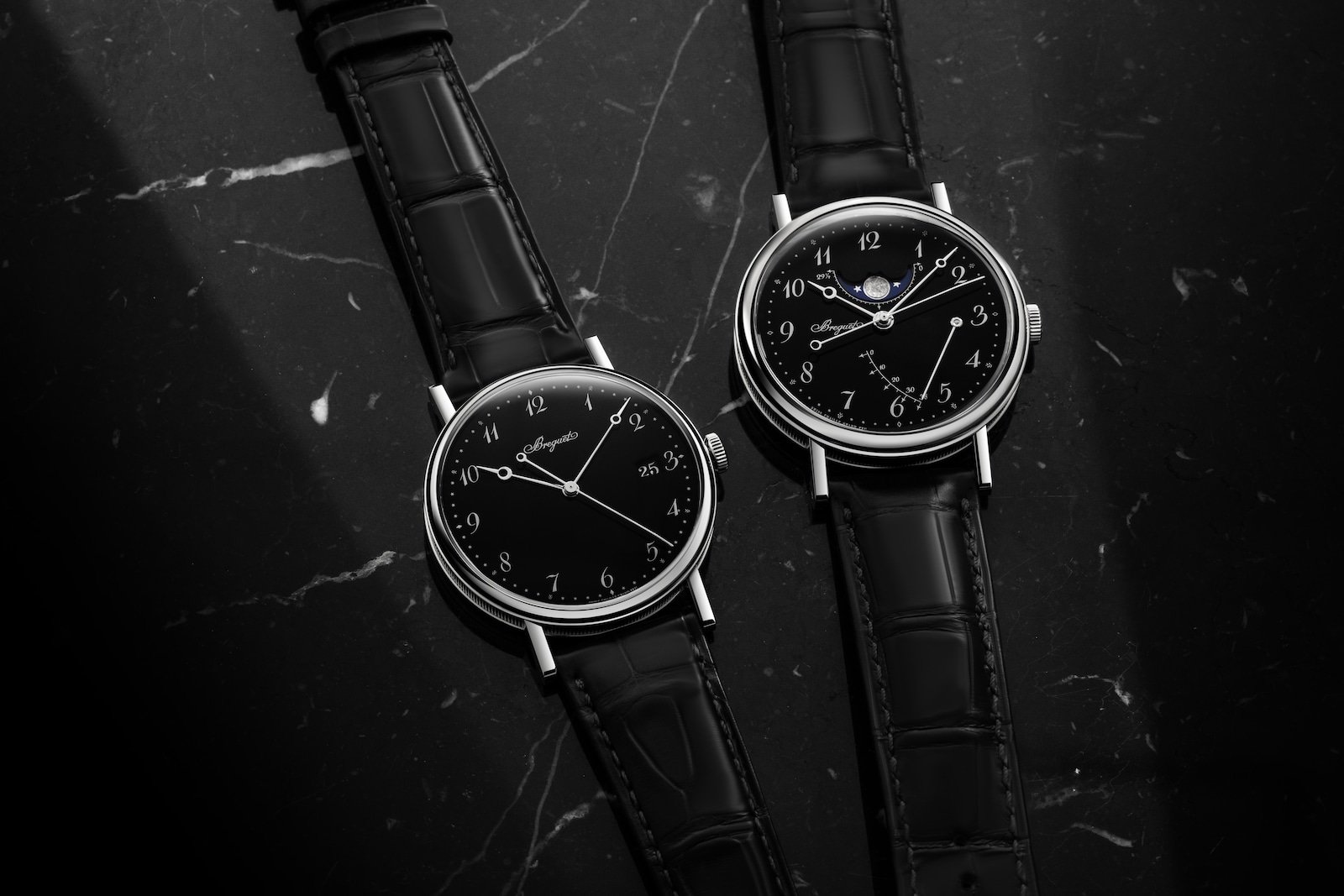 Two Breguet Classique watches with black dials on a dark stone surface.